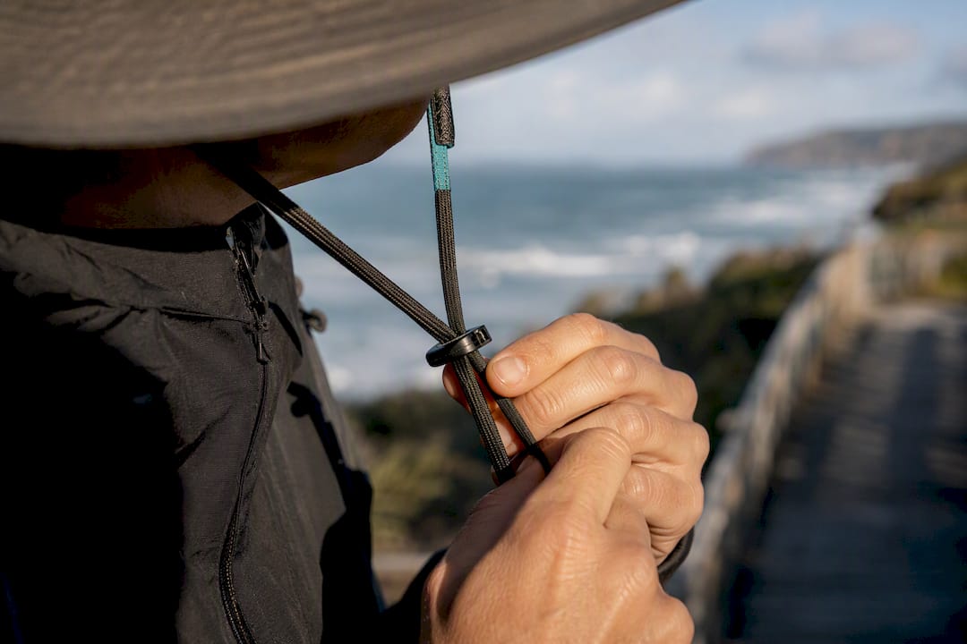Hand securing chin strap beneath hat brim
